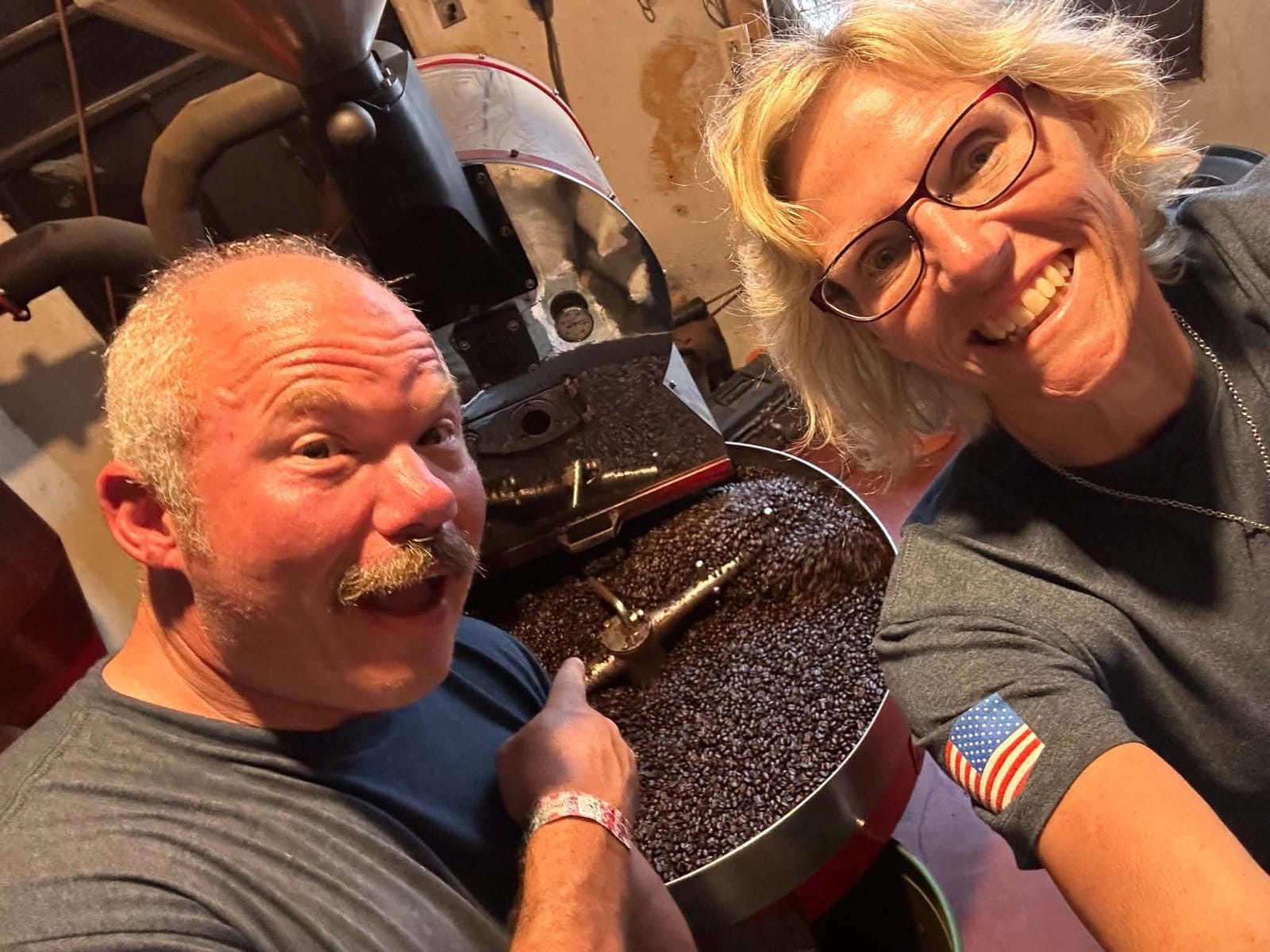 Chuck and Suzi Jones smiling beside their coffee roaster as fresh-roasted beans cool in the tray.