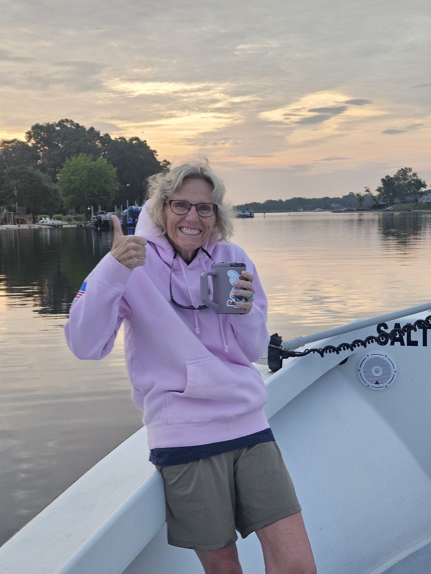 Suzi Jones on a boat at sunrise holding a First Cast coffee, calm water behind her.