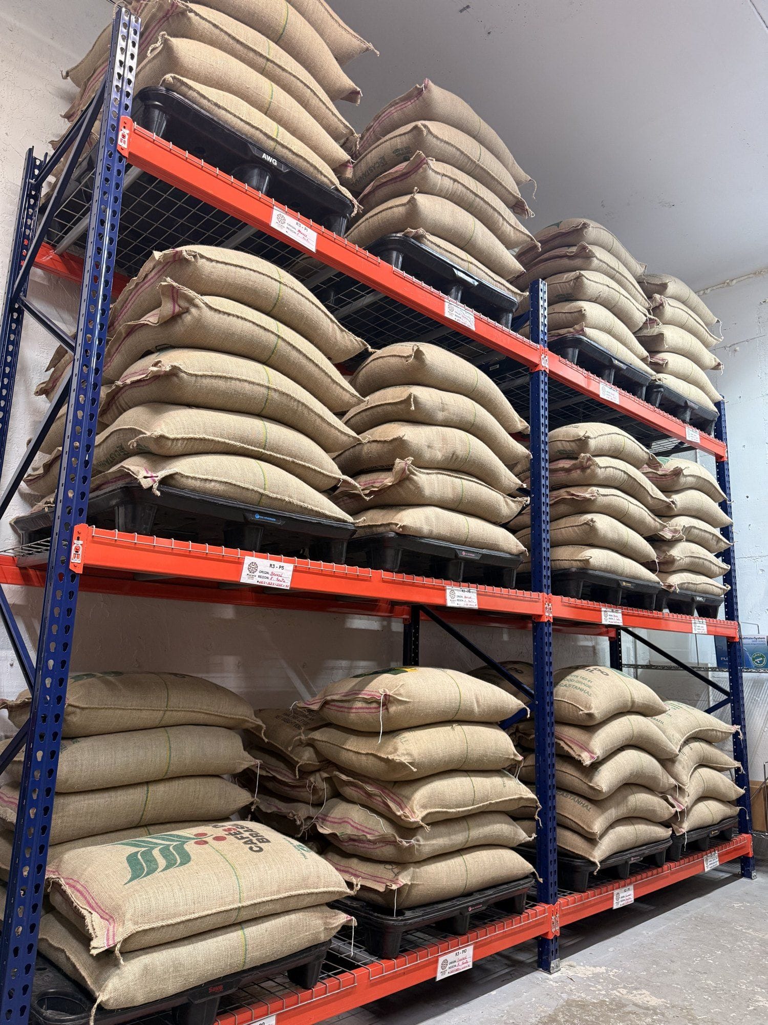 Jute bags of green coffee stacked on pallet racking at the Múcaro Coffees roastery.